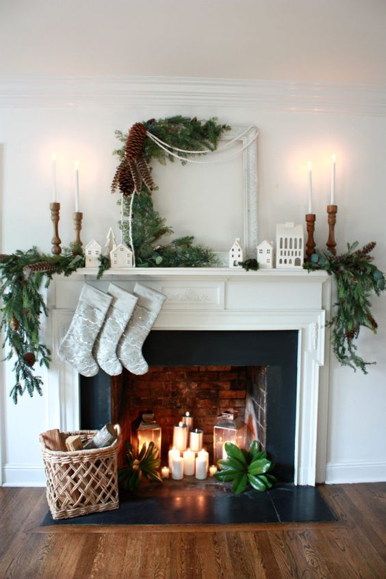 a lovely Christmas fireplace with pillar candles and candle lanterns, a basket with firewood, evergreens and tall and thin candles