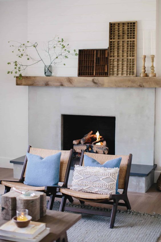 a mid-century modern living room with a concrete fireplace, woven chairs and a rug plus a mantel with chic decor