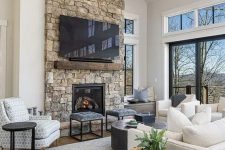 a modern chalet living room with a stone fireplace, neutral seating furniture, a coffee table and stools