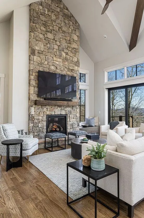 a modern chalet living room with a stone fireplace, neutral seating furniture, a coffee table and stools