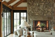 a modern chalet living room with a stone fireplace, neutral seating furniture, a stained side table and a console one