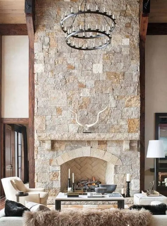 a modern chalet living room with a stone fireplace, neutral seating furniture, a tiered metal chandelier
