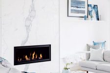 a modern coastal living room with a white marble fireplace, neutral furniture and blue accents for a beachy feel