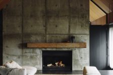 a modern industrial living room with an oversized concrete fireplace and a rough wooden mantel plus comfy furniture