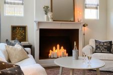 a modern living room with a fireplace with pillar candles, neutral seating furniture, a coffee table and artwork
