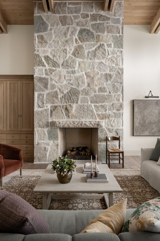 a modern living room with a stone fireplace, various muted color seating furniture, a low coffee table and some decor