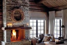 a moody neutral living room with a grey stone fireplace, vintage furniture, faux fur rugs and blankets and candles