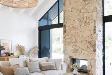 a neutral boho living room with a stone fireplace, a neutral sectional a low coffee table and a woven pendant lamp