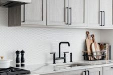 a neutral farmhouse kitchen with a white penny tile backsplash, black fixtures and a white marble kitchen island