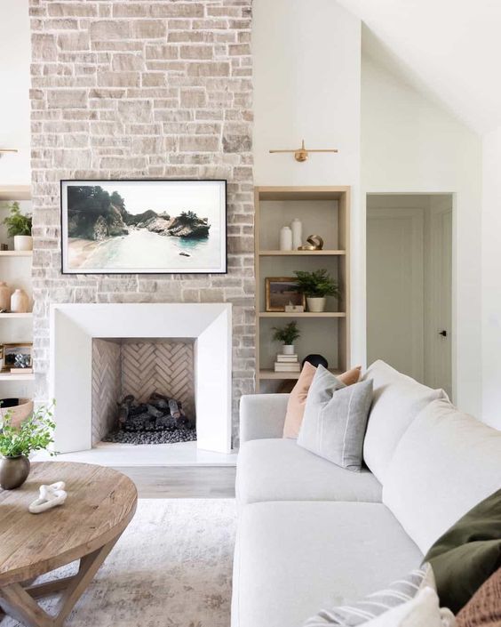 a neutral living room with a stone fireplace, a neutral sofa, muted color pillows, a stained coffee table and some decor