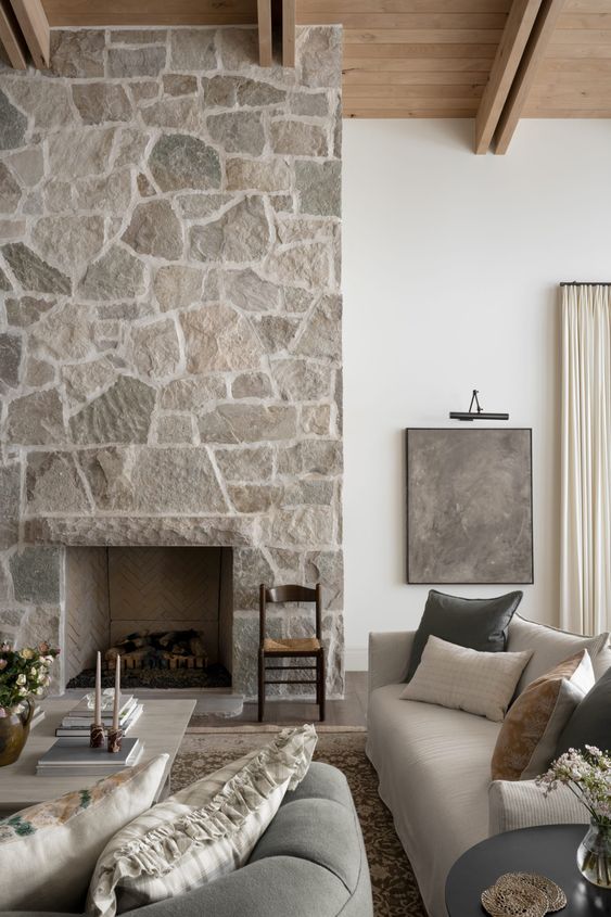 a neutral living room with a stone fireplace, neutral seating furniture, a coffee table and some decor