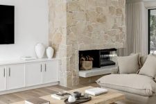 a neutral living room with a stone fireplace, neutral seating furniture, a low coffee table and white built-in cabinets