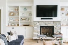 a neutral living room with built-in storage units, a stone clad fireplace, a TV, a navy sofa, tan seating furniture