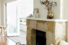 a neutral stone fireplace with a basket for firewood and a white mantel with candles, vases and blooms makes the space cozy and chic