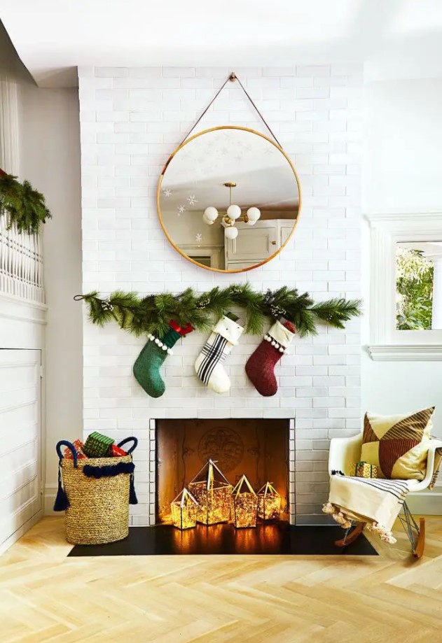 A non working fireplace styled for Christmas with some stockings hanging over it and with lights lanterns inside it