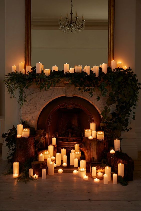 A non working fireplace with pillar candles, candles and greenery on the mantel and tree stumps is amazing