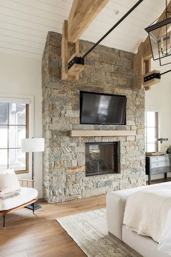 a ranch bedroom done with a rough stone fireplace with a wooden mantel matching the beams is a lovely and welcoming space