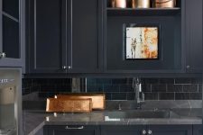 a refined moody kitchen in black, with grey marble countertops and a black subway tile backsplash is ultimately chic