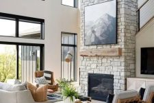 a refined ranch living room with a stone fireplace, wooden mantel and an artwork plus chic grey furniture