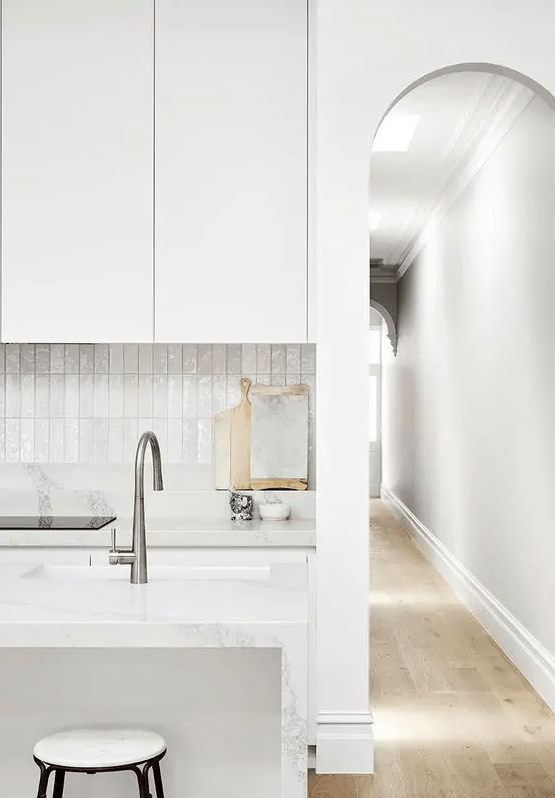 a refined white kitchen with sleek cabinets, a white stacked tile backsplash, a kitchen island and stainless steel fixutres