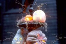 a rustic Halloween decoration of a stand with moss, branches, pumpkins and a large blackbird is very scary