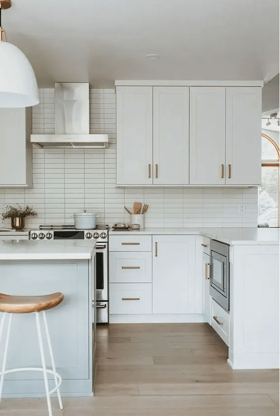 a serene white kitchen with a stacked tile backsplash, shaker cabinets, white countertops and wooden stools