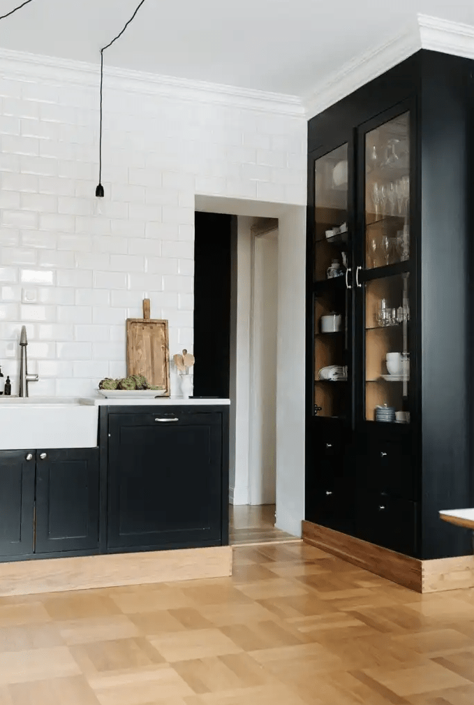 a sophisticated kitchen with hardwood floors, black shaker cabinets, white subway tiles on the wall