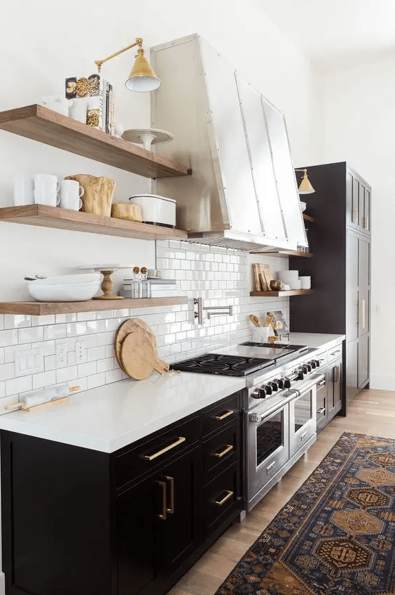 a stylish black farmhouse kitchen with white stone countertops, a whiet subway tile backsplash, open shelves and a large metal hood