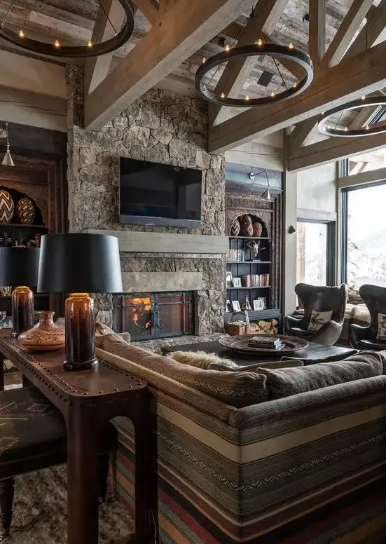 a stylish chalet living room clad with wood, with a stone fireplace, boho and modern furniture and round chandeliers