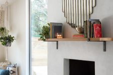 a stylish modern concrete fireplace with a mantel with books and a catchy mirror over it plus a bench next to it