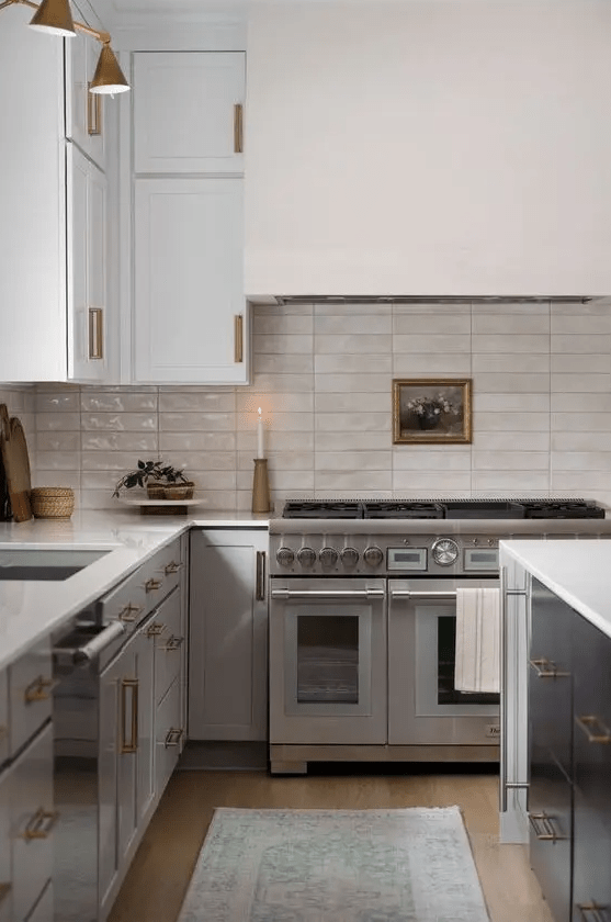 a stylish two-tone kitchen with a white stone countertops and a stacked tile backsplash plus brass fixtures