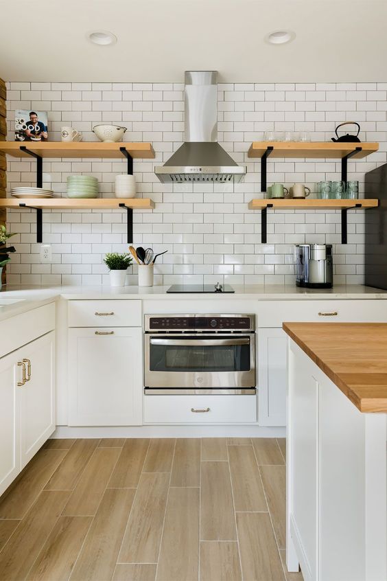 a stylish white Scandinavian kitchen with shaker cabinets, stone and butcherblock countertops, a white subway tile wall and shelves