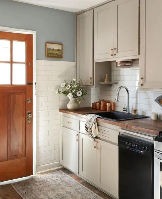 a tan farmhouse kitchen with shaker cabinets, butcherblock countertops, brass handles and white subway tiles over two walls