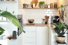 a tiny minimalist kitchen in white, with wooden coutnertops and a shelf plus a white subway tile backsplash and pendant bulbs