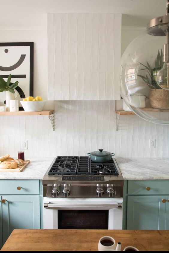 a turquoise kitchen with white stone countertops, a white stacked tile wall and a hood is amazing