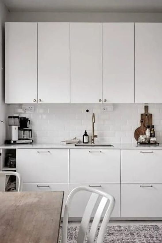 a white Nordic kitchen with white countertops and a white subway tile backsplash and simple dining furniture