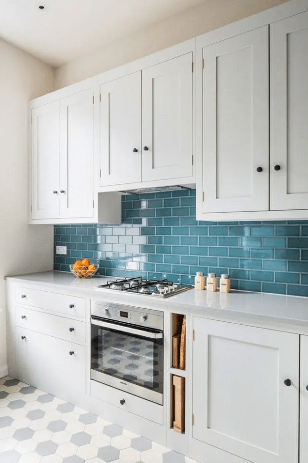 a white Scandinavian kitchen with shaker cabinets, a bold blu subway tile backsplash and white countertops