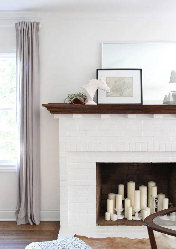 a white brick fireplace with pillar candles, some elegant decor on the mantel is super chic and cool