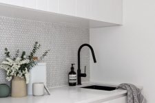 a white kitchen with a white penny tile backsplash and black fixtures for an ultra-modern look