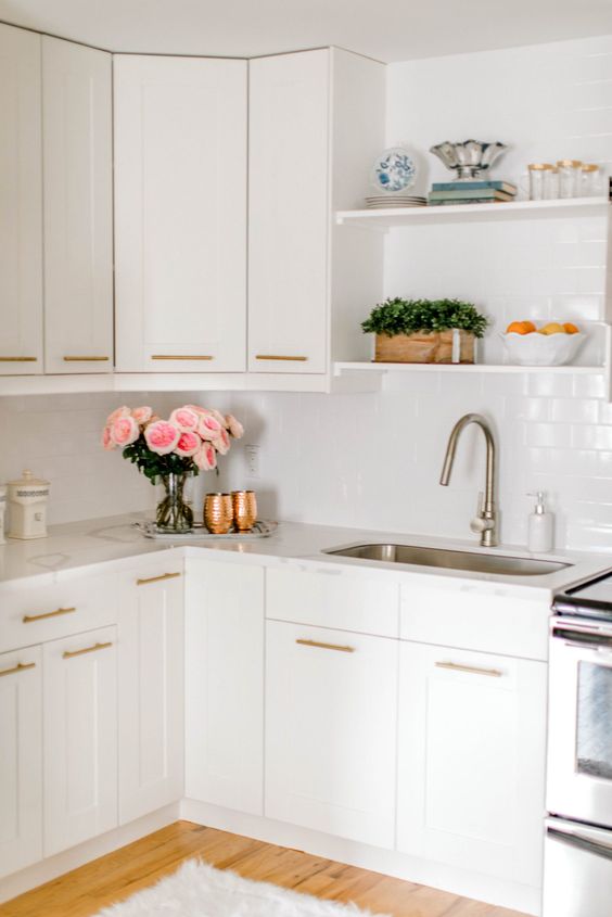 a white kitchen with a white subway tile backsplash and white countertops plus gold fixtures is a lovely space