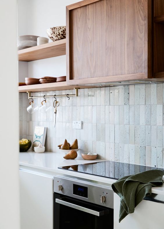 a white kitchen with stained shelves and a stained hood, a whimsical Zellige stacked tile backsplash and brass fixtures