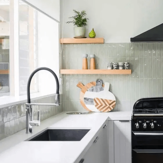 a white kitchen with white countertops, a light green stacked tile backsplash, black fixtures and appliances for a touch of drama