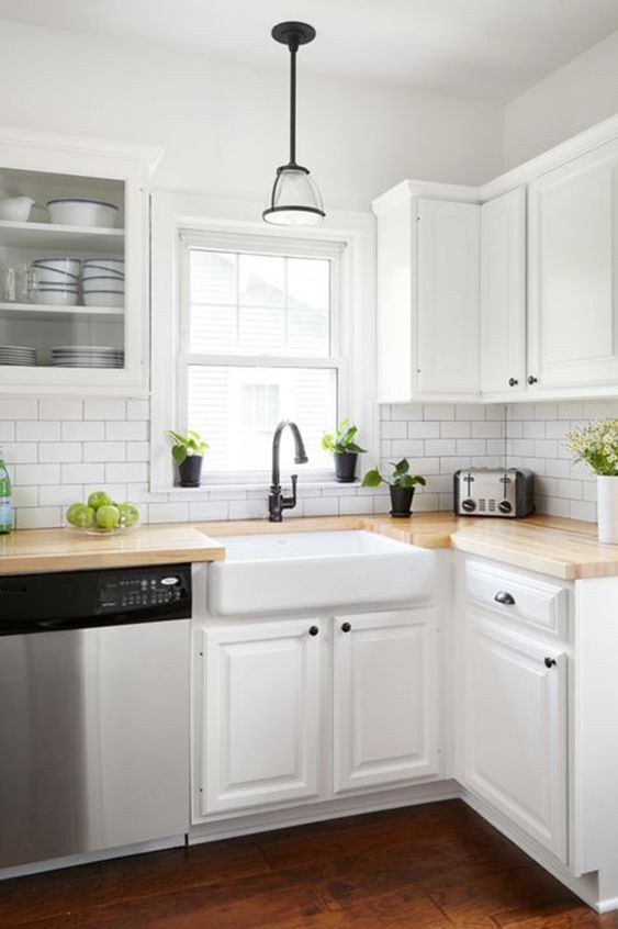 a white modern farmhouse kitchen with butcherblock countertops, white subway tiles, black touches for creating a contrast