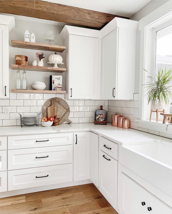 a white modern farmhouse kitchen with shaker cabinetry, white stone countertops and a white subway tile backsplash plus stained wood