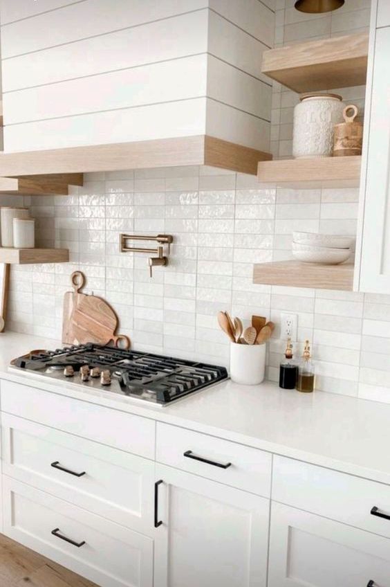 a white modern farmhouse kitchen with shaker cabinets, a glossy white stacked tile backsplash and stained shelves