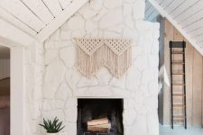 a white stone boho fireplace with macrame and potted greenery is a cool and chic idea for a neutral space
