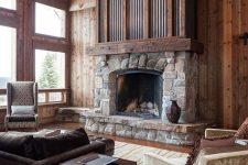 an elegant and chic cabin living room with rich stained woods, a stone and metal fireplace and vintage furniture
