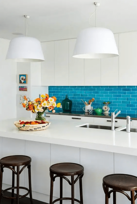 an eye catchy kitchen with sleek cabinets, a bold blue subway tile backsplash, a large kitchen island and dark stools