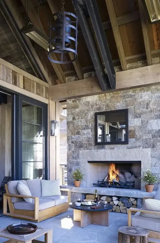 an outdoor space under a roof, with a stone fireplace, neutral modern furniture, metal pendant lamps and a low coffee table is chic