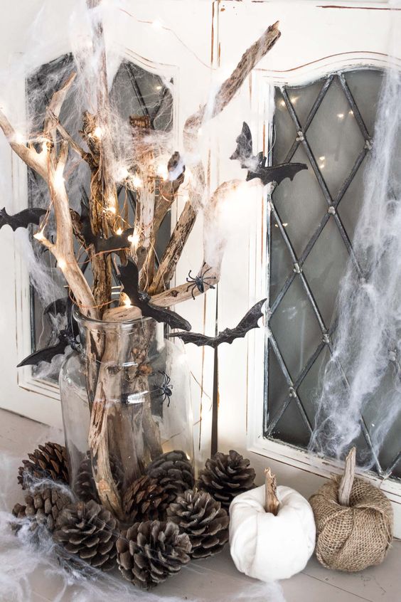 rustic Halloween decor of branches with lights, spiderweb and bats, pinecones and fabric pumpkins near the vase